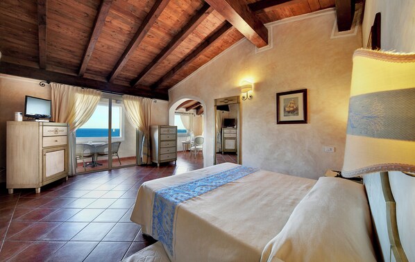 A bedroom with a bed, a desk, and a chair, a bathroom with a mirror and a sink, and a view of the sea through a window.