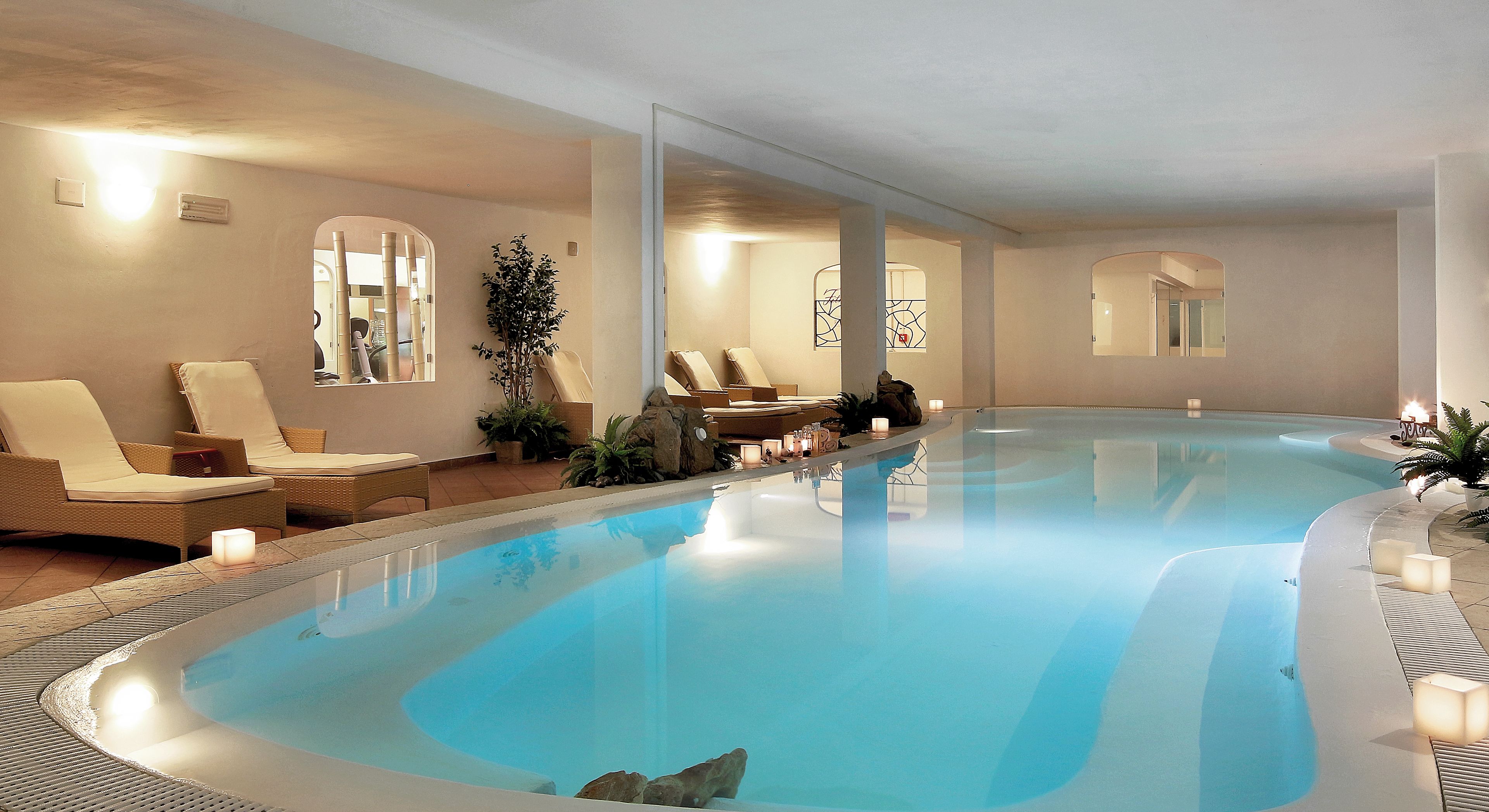 Una piscina interior amplia con sillones de descanso y velas a lo largo del borde.