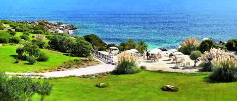 A coastal landscape with a paved walkway, beach chairs, and umbrellas.
