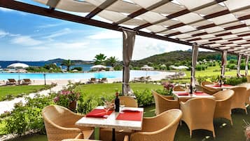 An outdoor patio with wicker furniture, tables with red napkins, and a view of a pool and greenery.