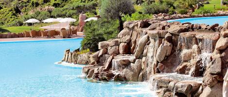 A pool with a rocky waterfall feature, surrounded by lounge chairs and umbrellas.