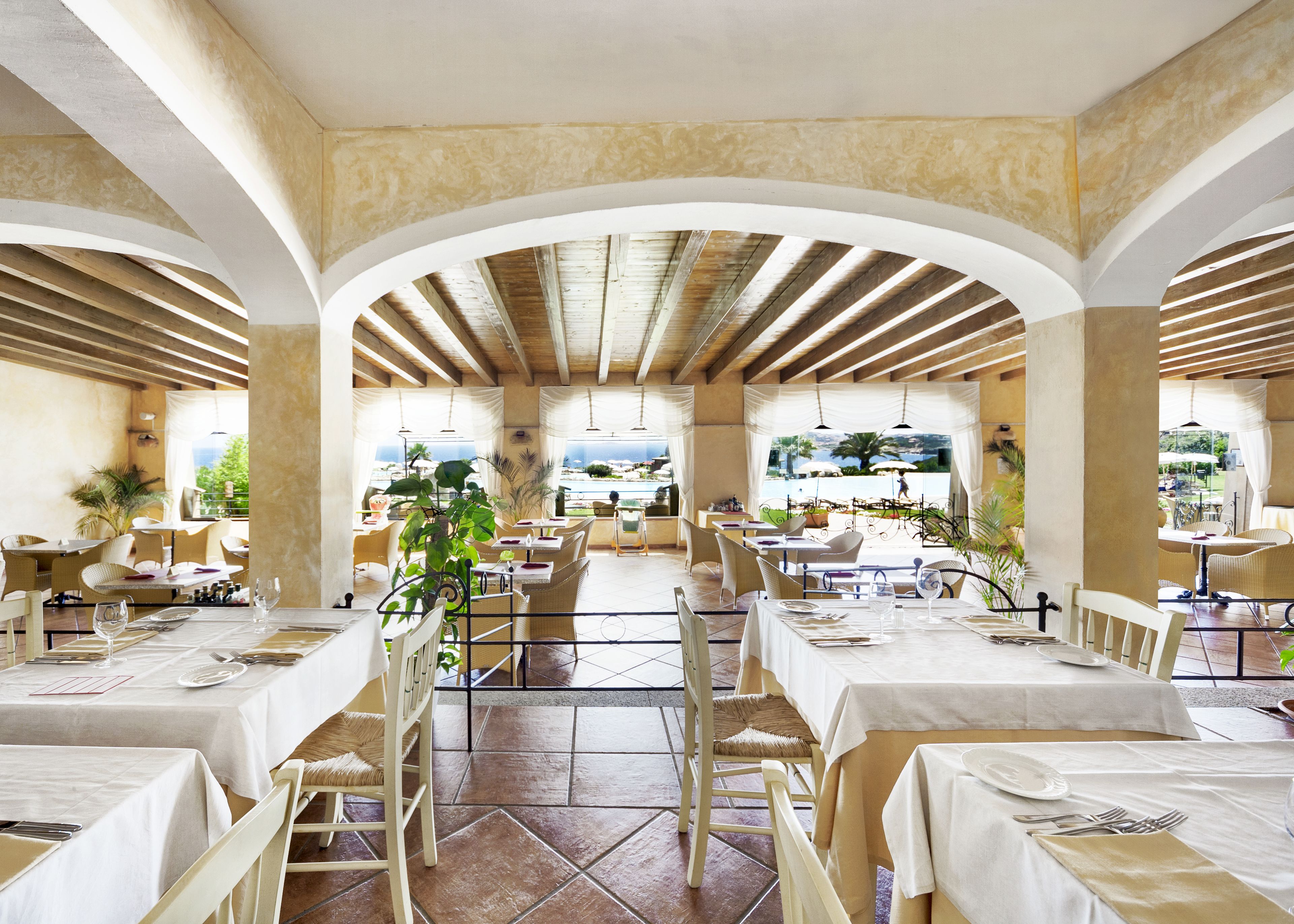 A spacious restaurant with multiple tables and chairs, large windows, and a view of the sea.