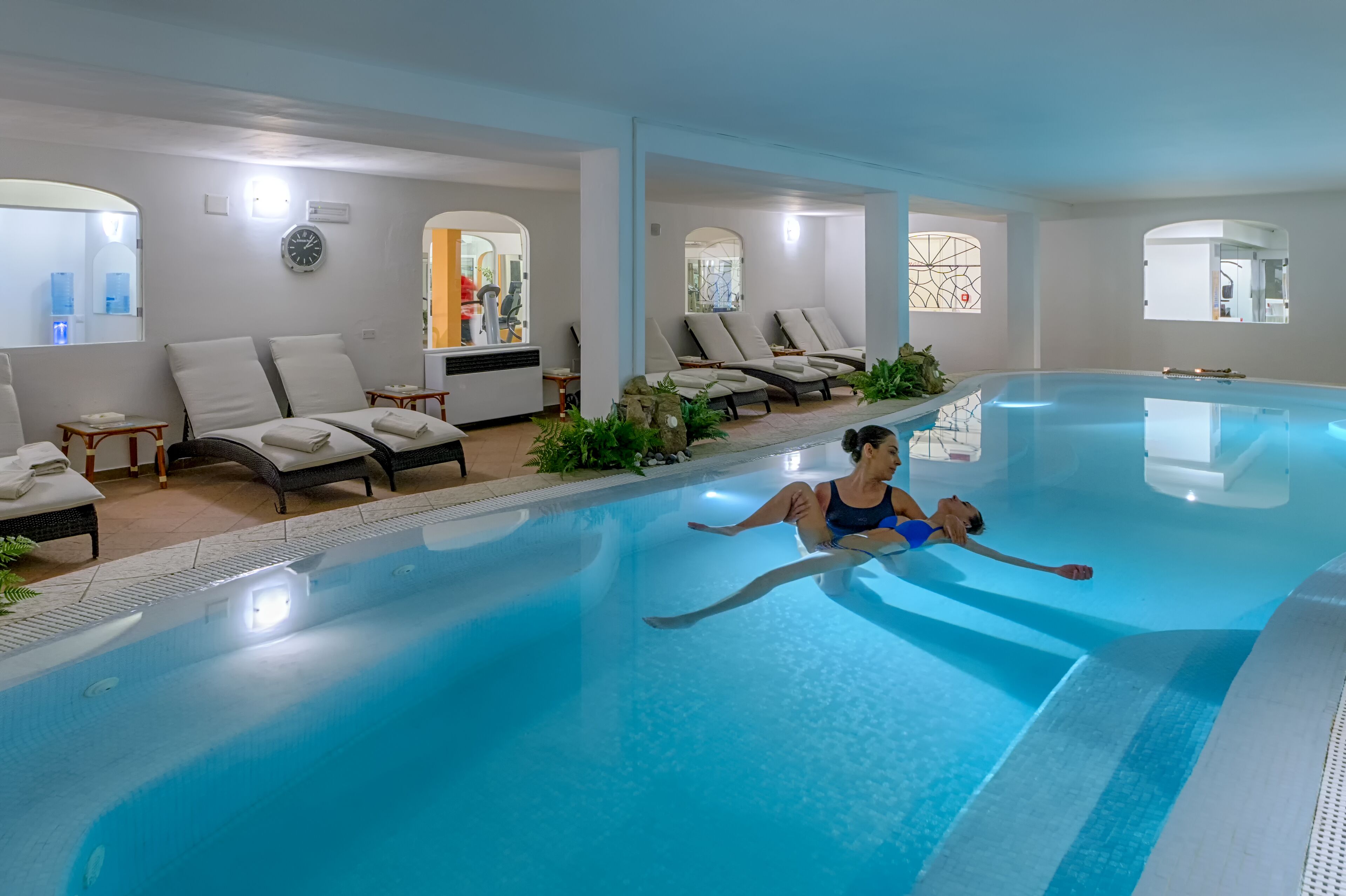 An indoor swimming pool with lounge chairs and a spa area.