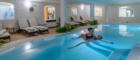 An indoor swimming pool with lounge chairs and a spa area.