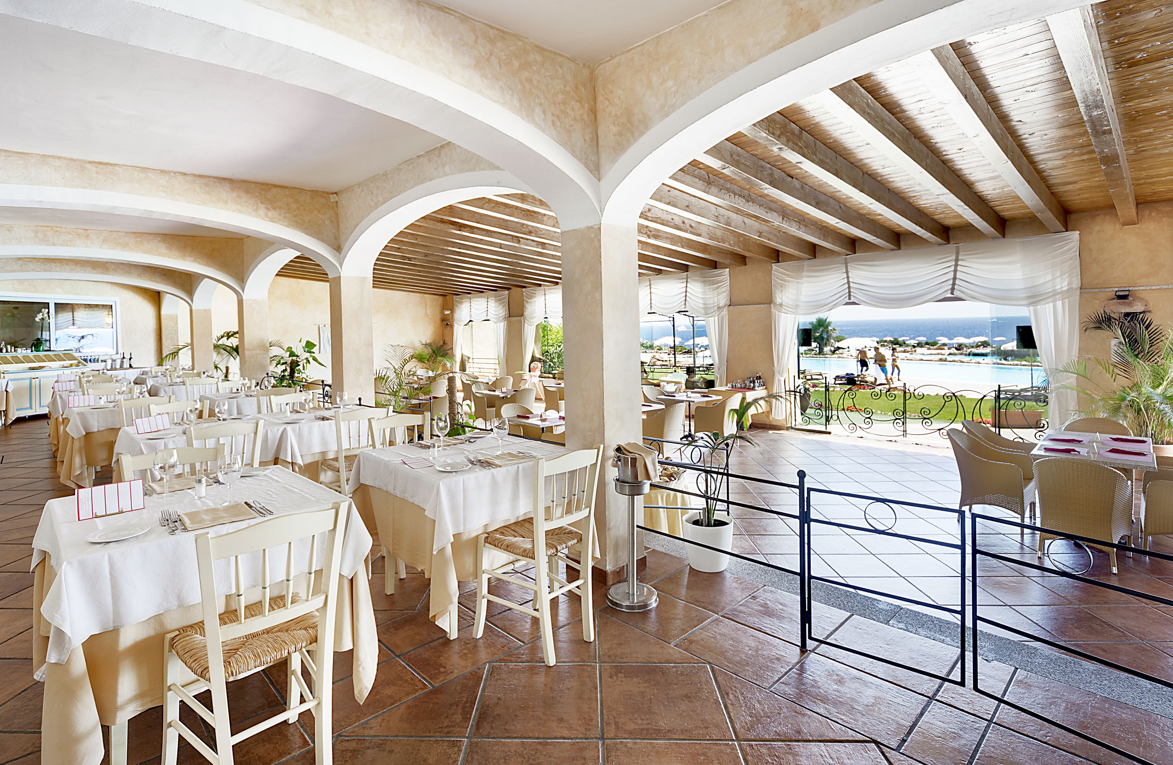 Un comedor amplio con varias mesas y sillas, vista a la piscina y un patio cubierto.