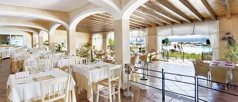 Un comedor amplio con varias mesas y sillas, vista a la piscina y un patio cubierto.
