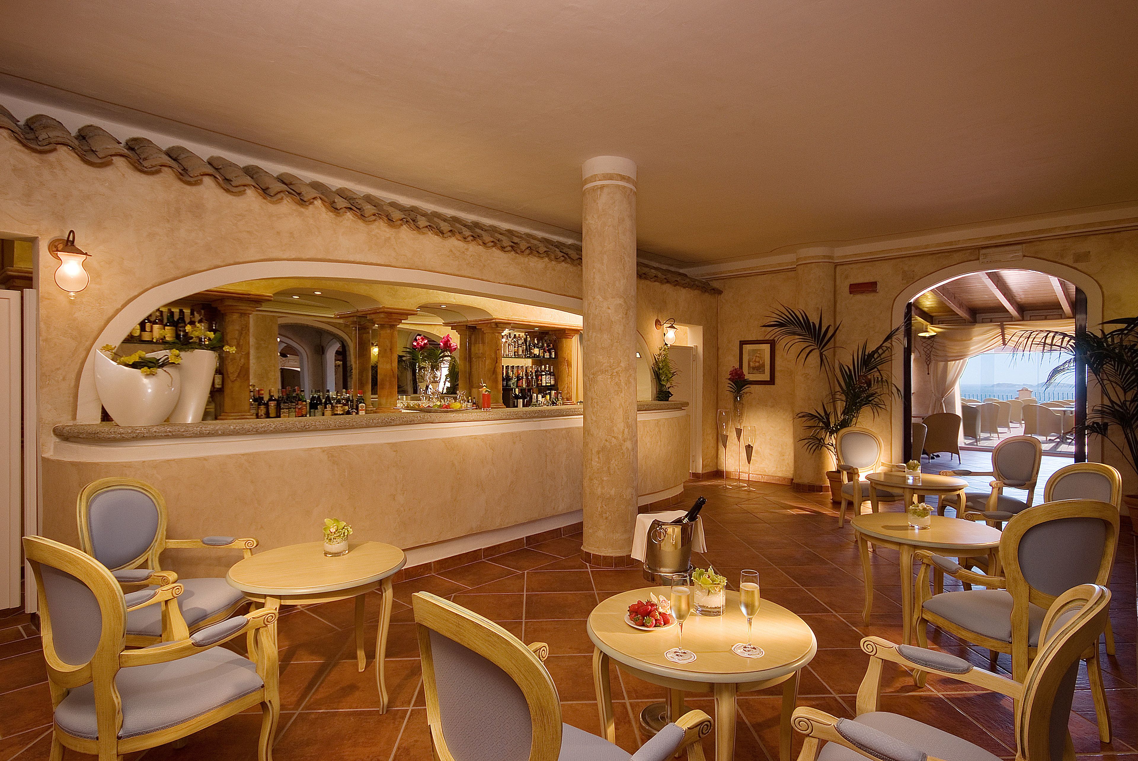 A bar area with multiple seating options, including round tables and chairs, and a bar counter with various bottles and a wine cooler.