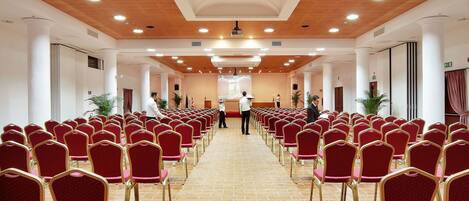 Un salón de conferencias con filas de sillas rojas y un escenario al frente.
