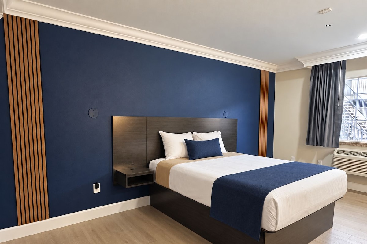 A modern hotel room with a large bed, a nightstand, and a window with curtains.