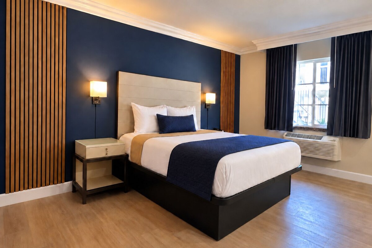 A hotel room with a bed, bedside tables, a wall-mounted lamp, and a window with curtains.