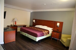 Una habitación de hotel con cama, escritorio, silla y mesita de noche.