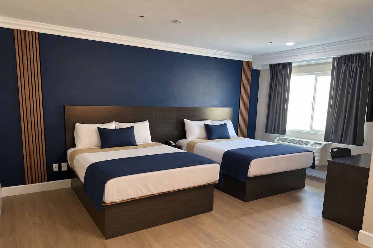 A hotel room with two beds, a desk, and a window with curtains.