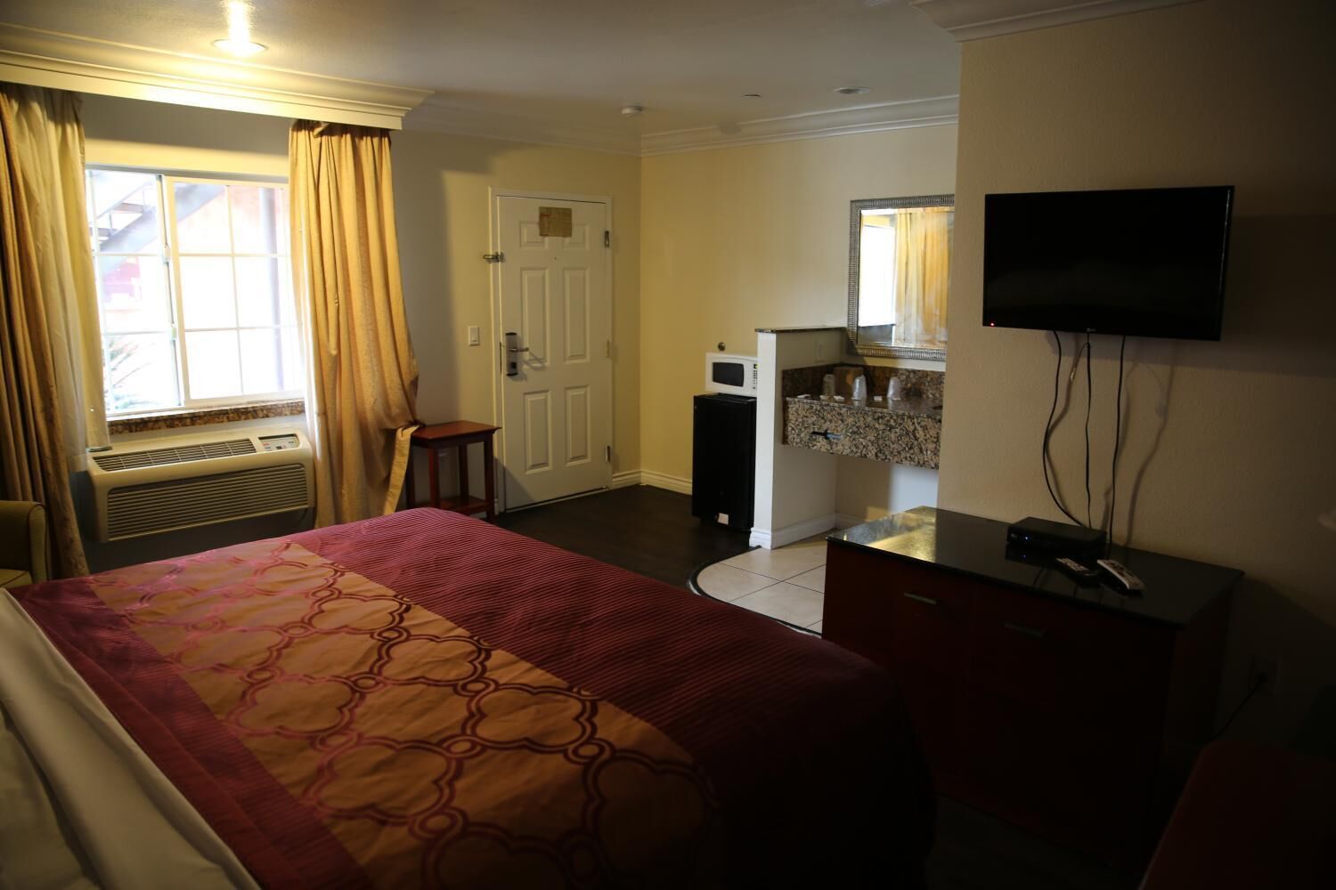 Quarto de hotel com cama, escrivaninha, televisão, micro-ondas e janela com cortinas.