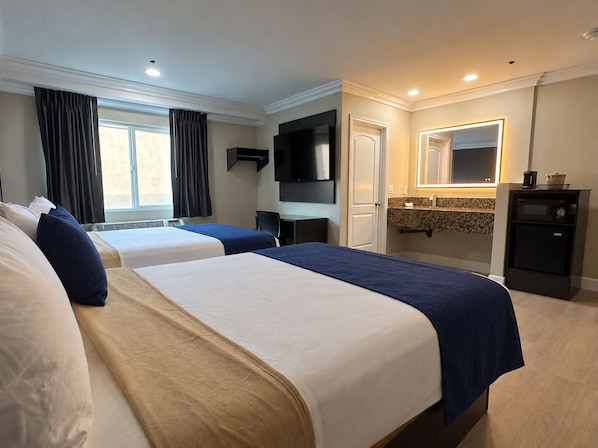 A hotel room with two beds, a flat-screen TV, a small desk, a mirror, and a minibar.