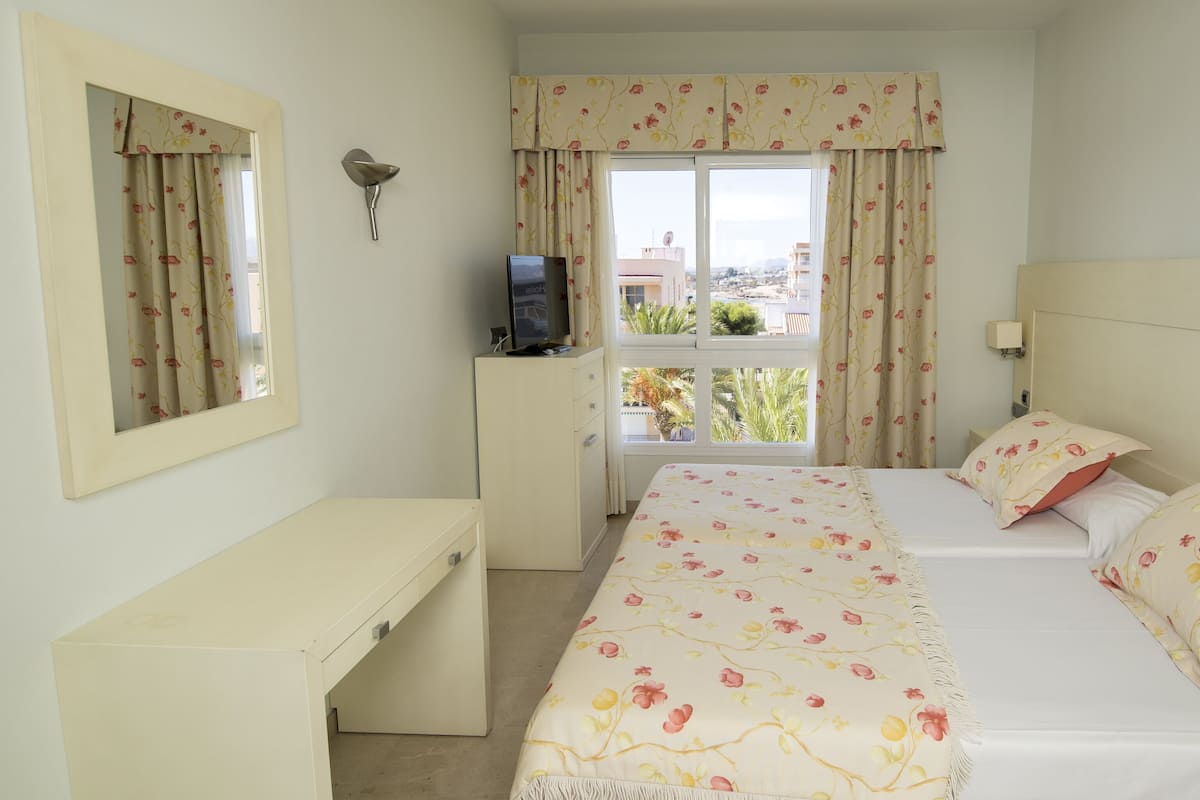 A bedroom with a bed, a desk, a mirror, and a window with curtains.