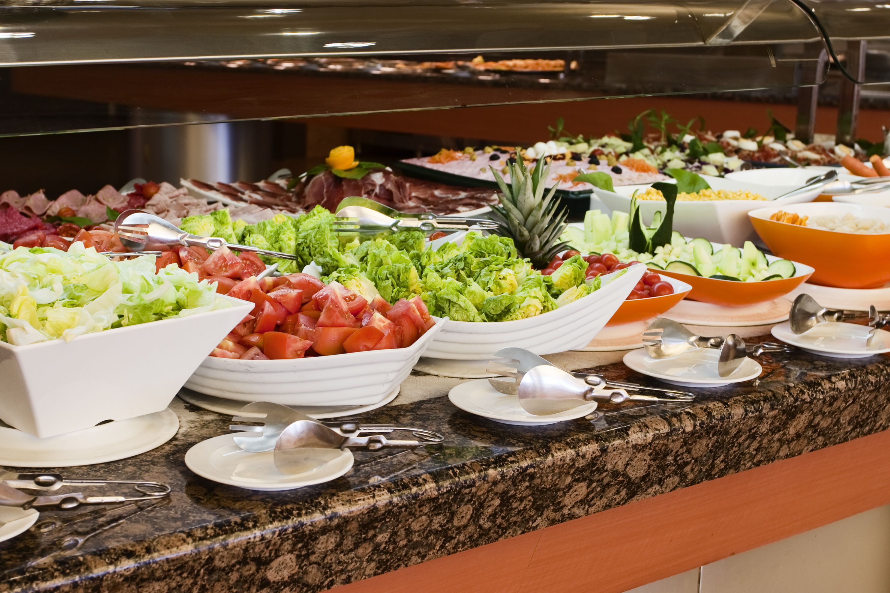 A buffet with various food items including salads, fruits, and meats.