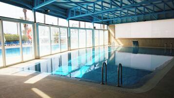 Une piscine intérieure avec des parois en verre transparent, un sol carrelé et un plafond en métal bleu.