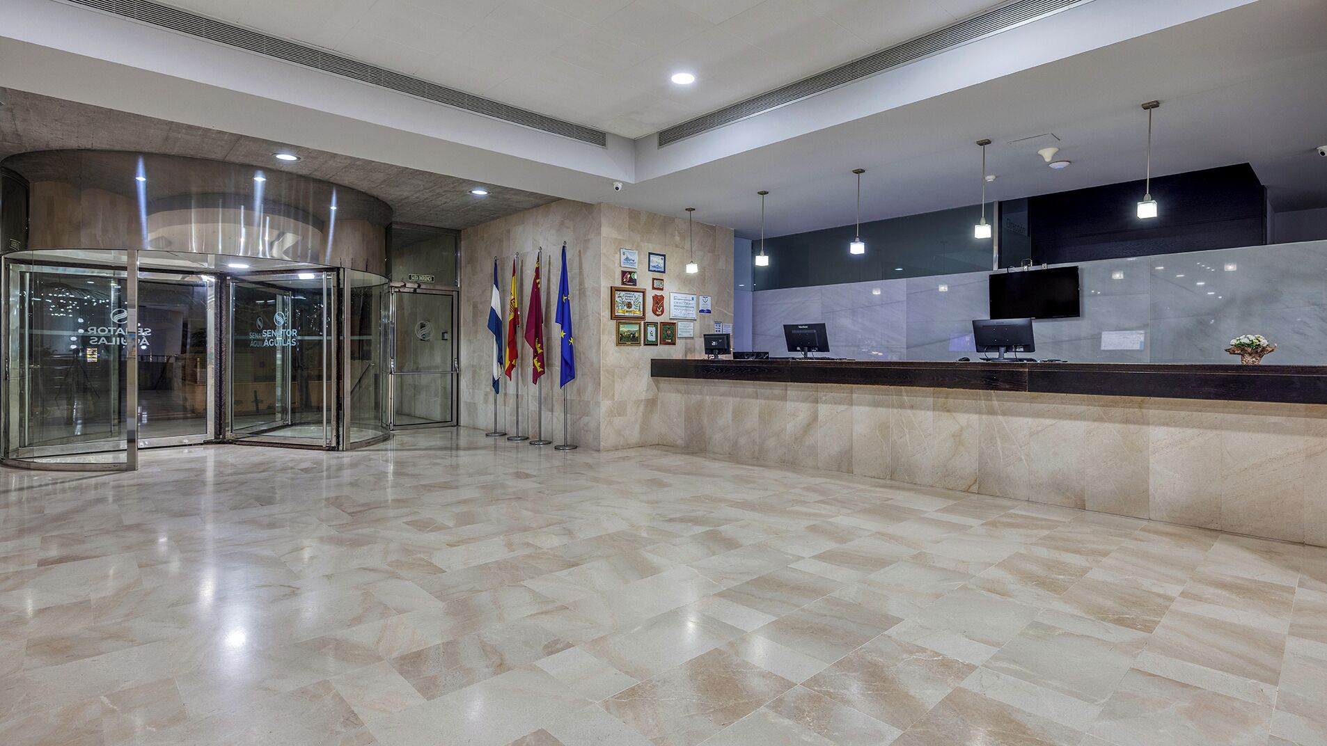 A modern reception area with a marble floor, glass revolving doors, and a reception desk with computers.