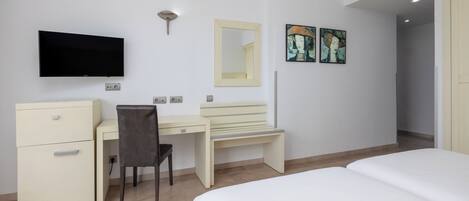 Una habitación de hotel con cama, escritorio con silla, televisión, espejo y obras de arte en la pared.