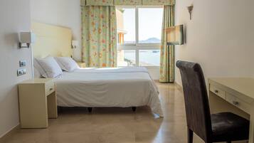 Habitación de hotel con cama, escritorio, silla, televisor y ventana con cortinas.