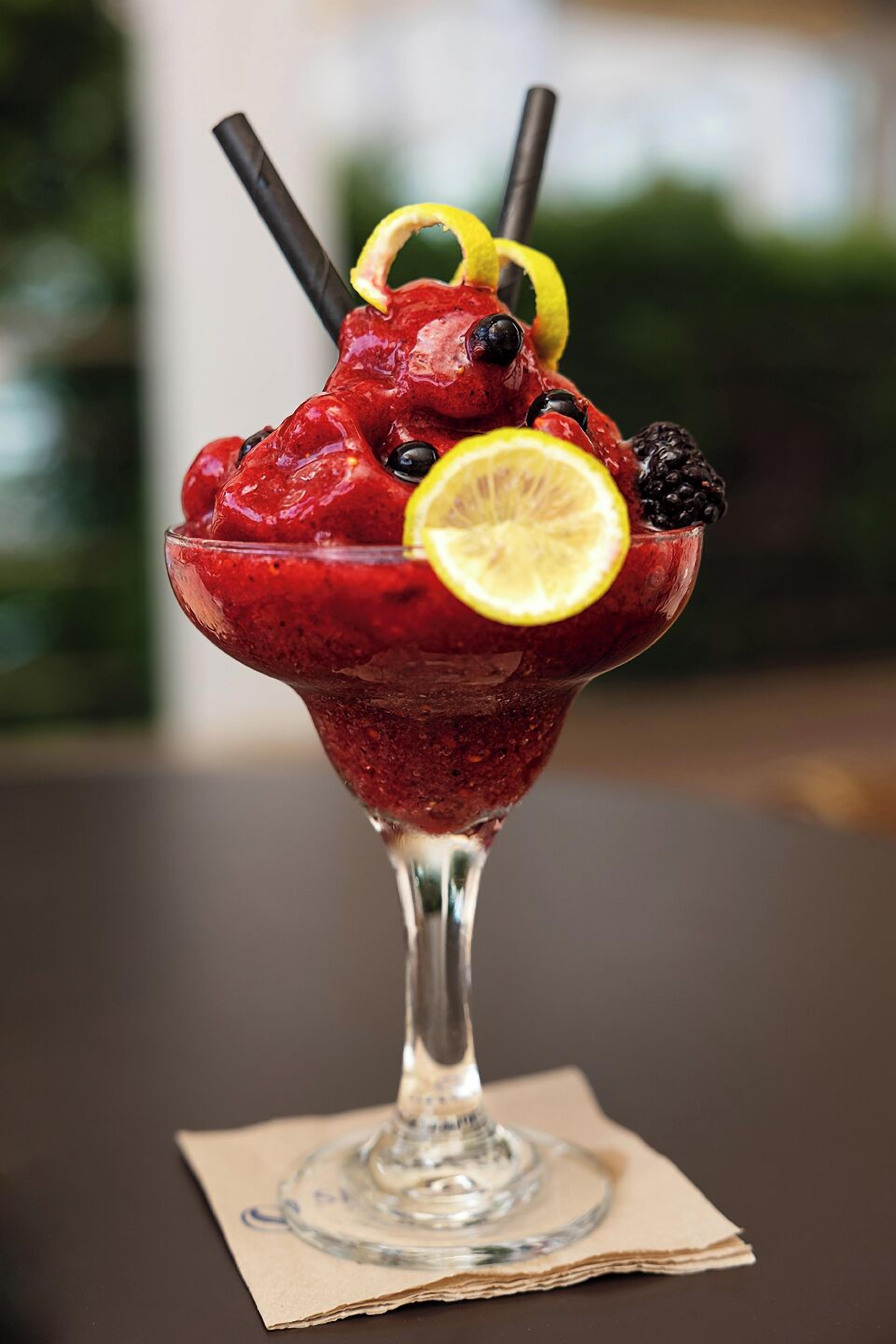 A cocktail in a glass with a lemon slice and blackberries on top.