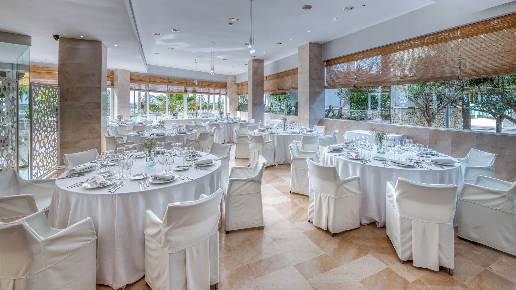 Un comedor espacioso con mesas redondas dispuestas para un evento formal, con manteles blancos y sillas.