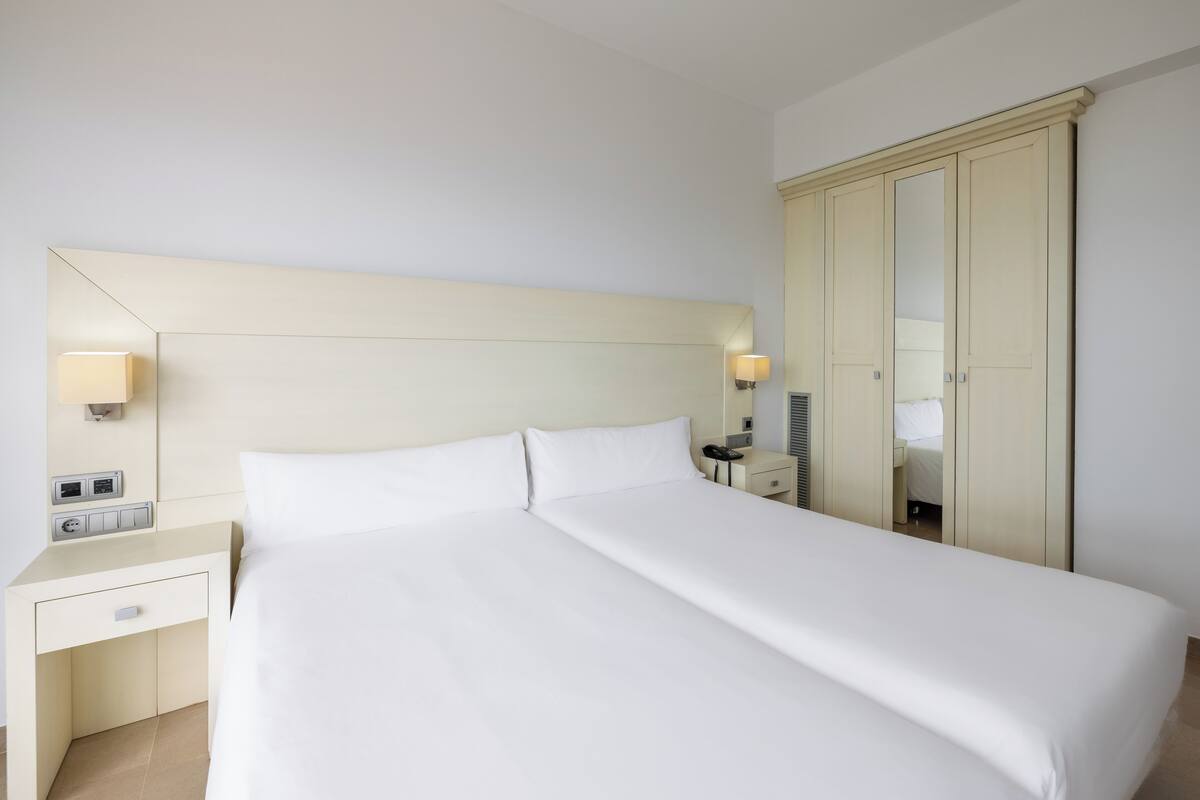 A neatly made bed with white linens, a bedside table with a lamp, and a wardrobe with a mirror.