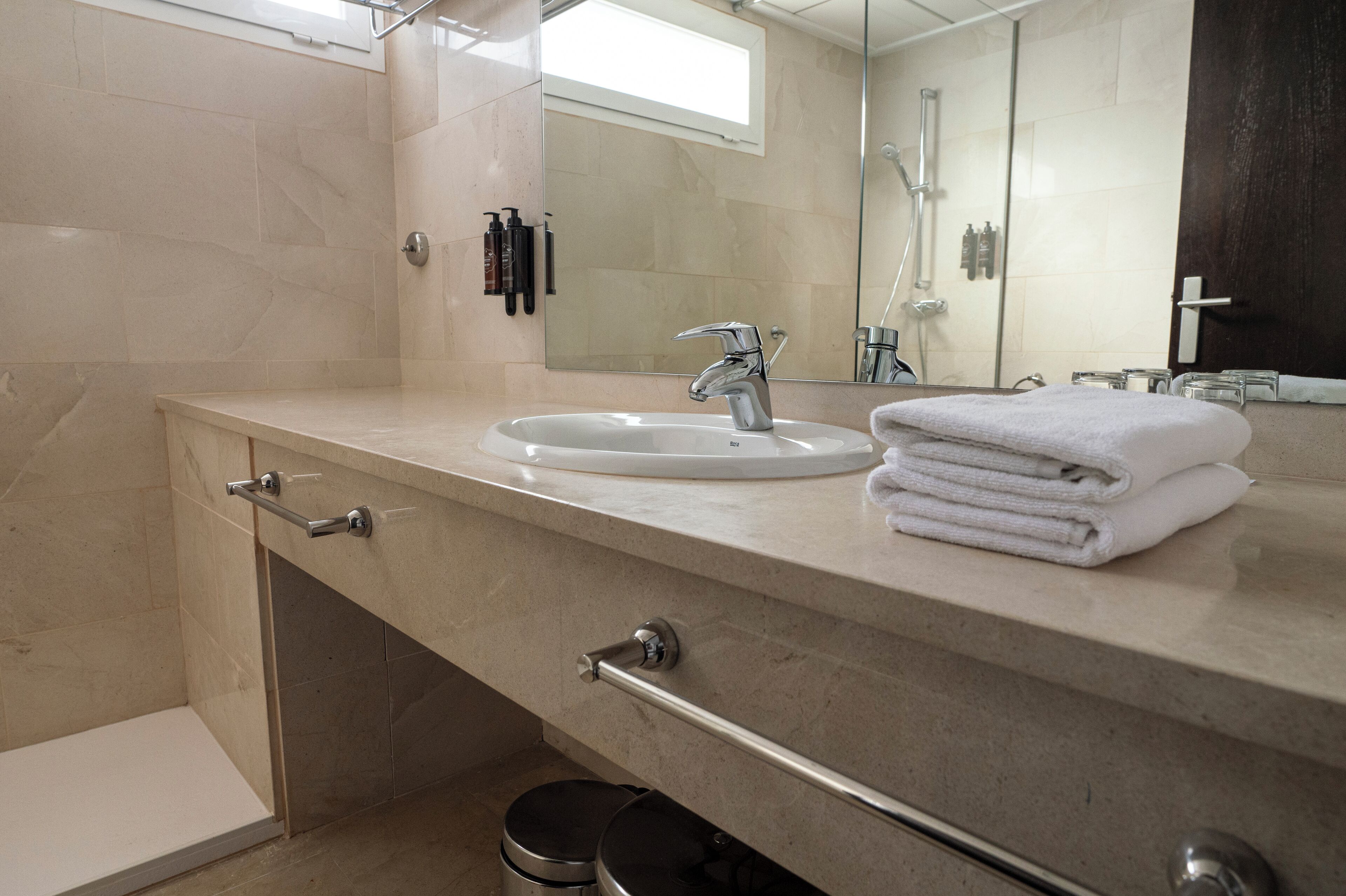 A modern bathroom with a sink, mirror, and towel stack.