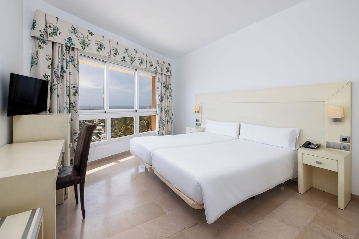 A hotel room with a bed, a desk, a chair, a TV, and a window with curtains.