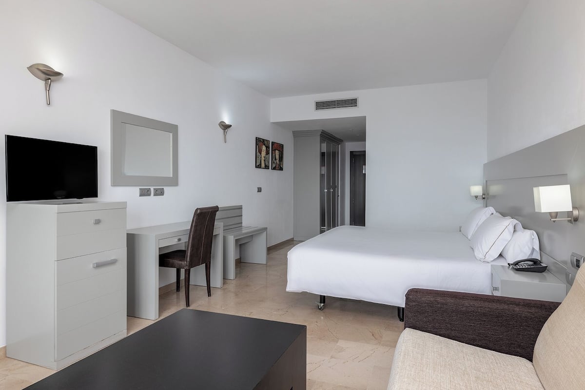 A modern hotel room with a bed, a desk, a television, a wardrobe, and a bathroom.