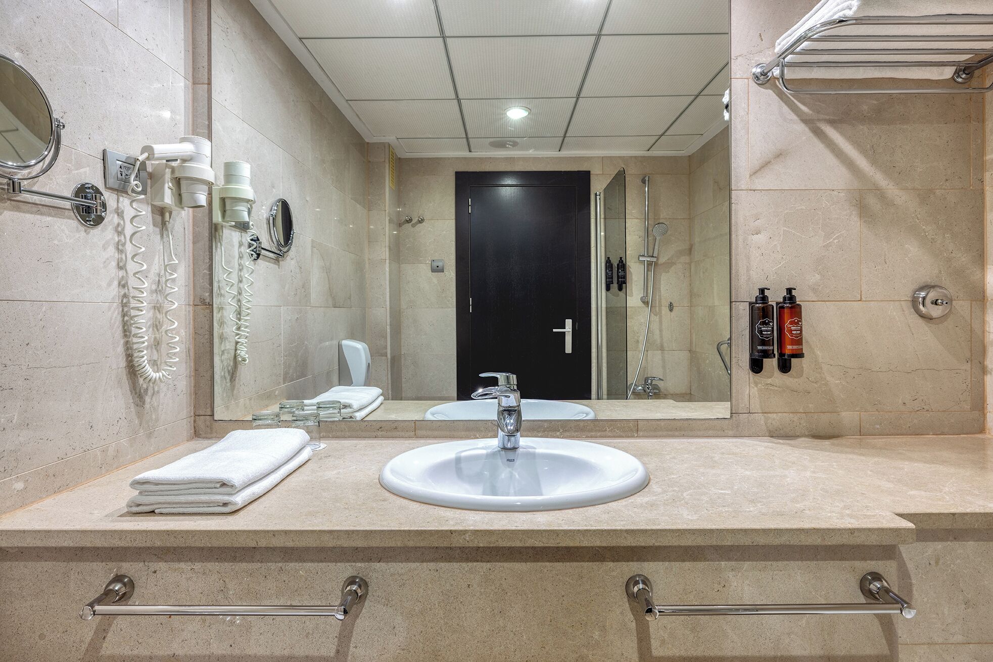 A modern bathroom with a sink, mirror, towel rack, and toiletries.