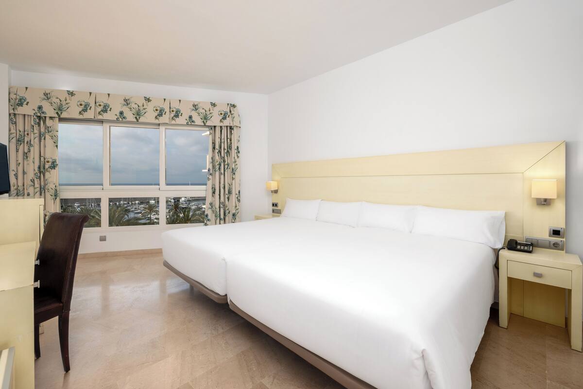 A hotel room with a large bed, a desk, a chair, and a window with curtains.