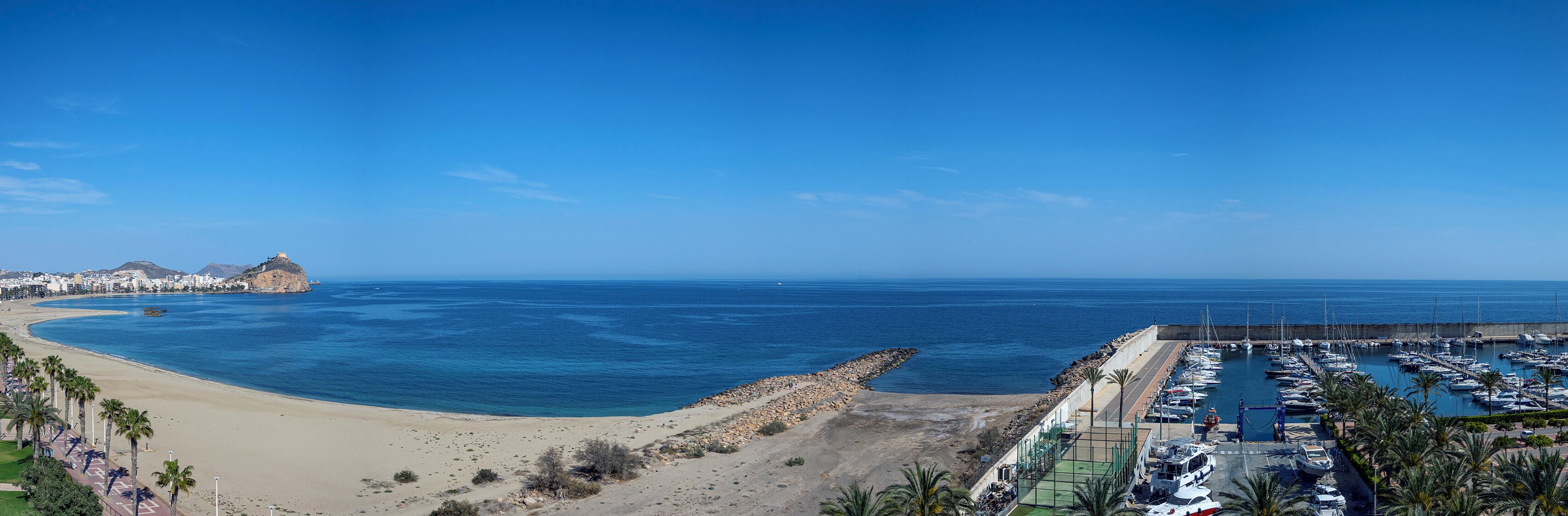 A coastal marina with boats docked, a sandy beach, and a rocky outcrop.