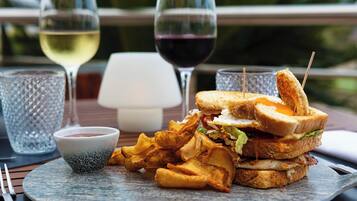 Una comida que incluye un sándwich, papas fritas y un pequeño recipiente con salsa, junto con dos copas de vino sobre una mesa.