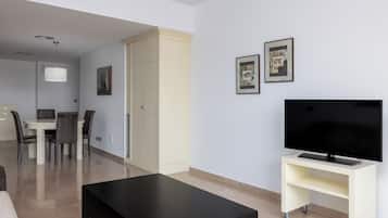 Una sala de estar moderna con una televisión de pantalla plana sobre un mueble, una zona de comedor con mesa y sillas, y un armario.