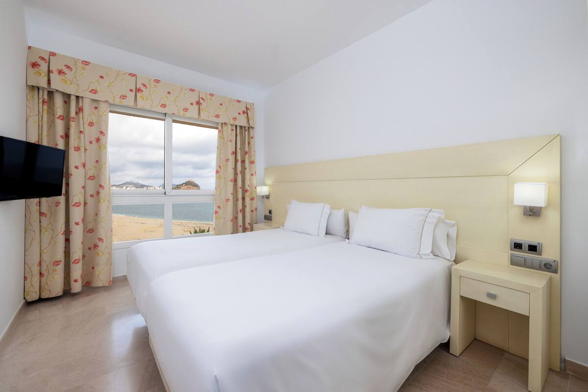 A hotel room with a large bed, a bedside table with a lamp, and a TV mounted on the wall.