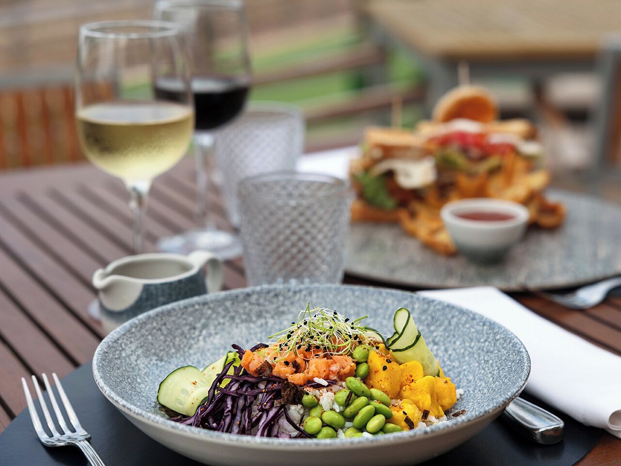 A dining table with a plate of food, a glass of white wine, and a cup of coffee.