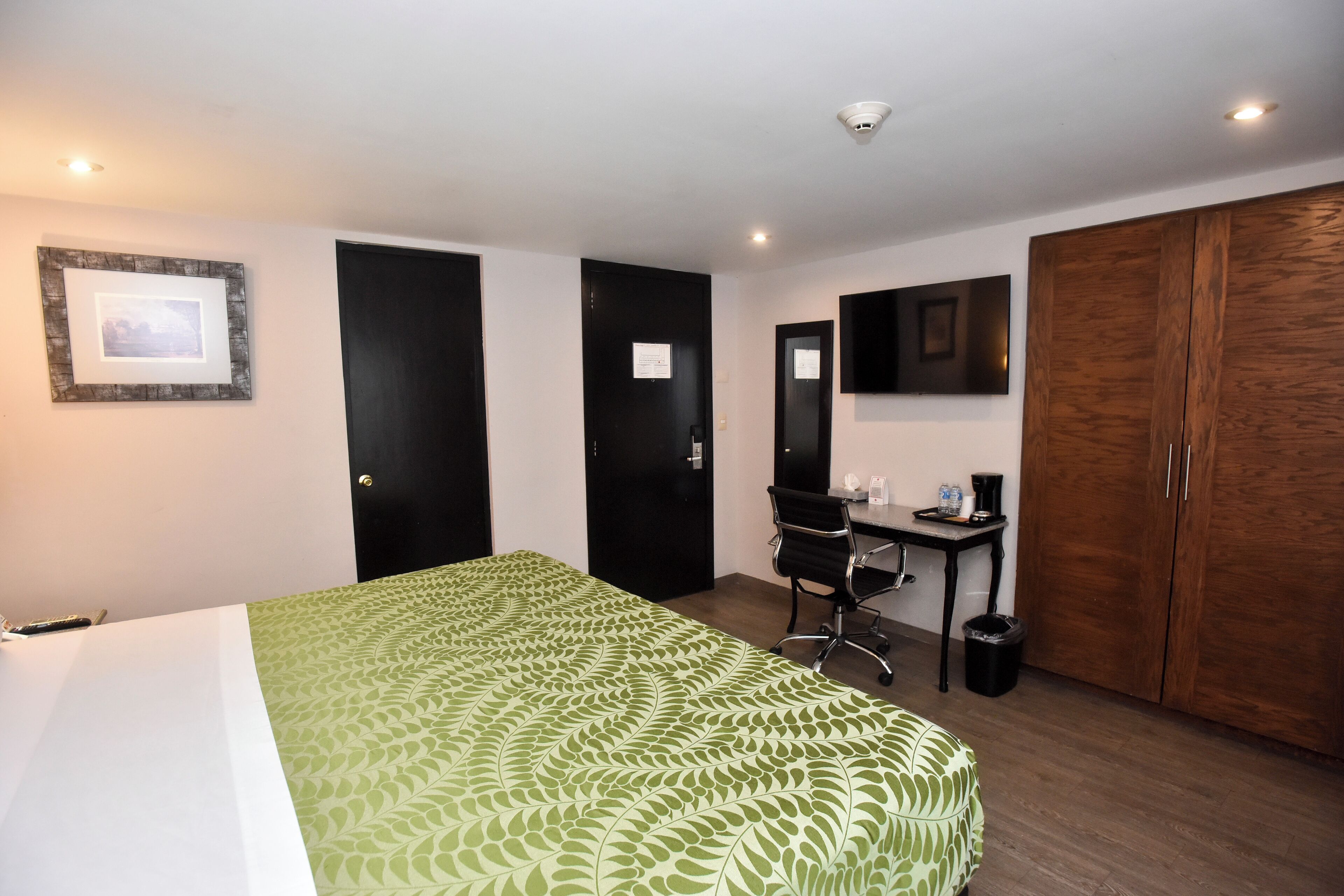 A hotel room with a bed, desk, chair, wardrobe, and a mounted TV.