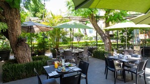 An outdoor dining area with tables and chairs, surrounded by greenery and umbrellas. - Plaza Camelinas Hotel (Querétaro)
