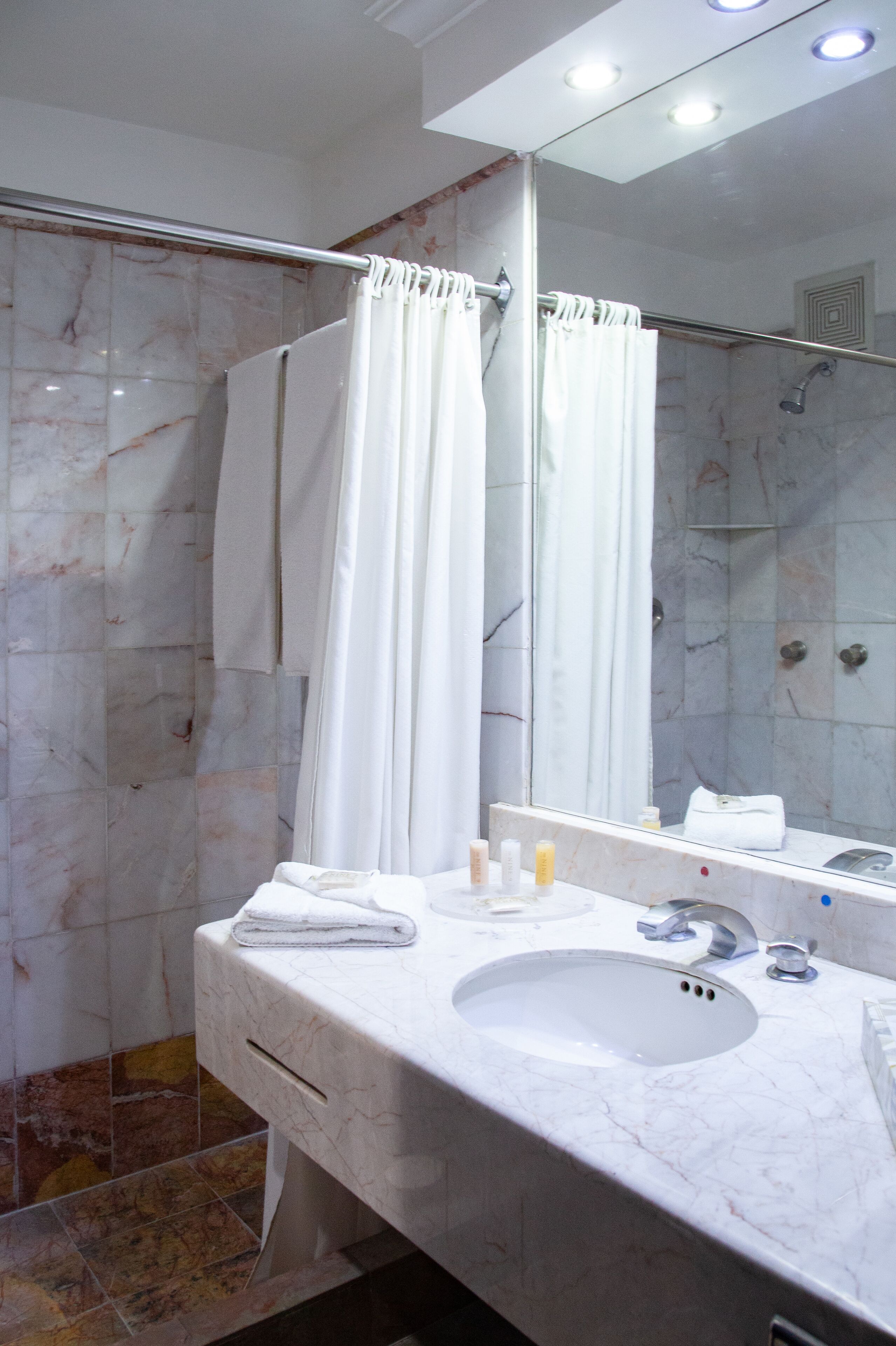 A bathroom with a marble sink, a glass shower enclosure, and a large mirror.