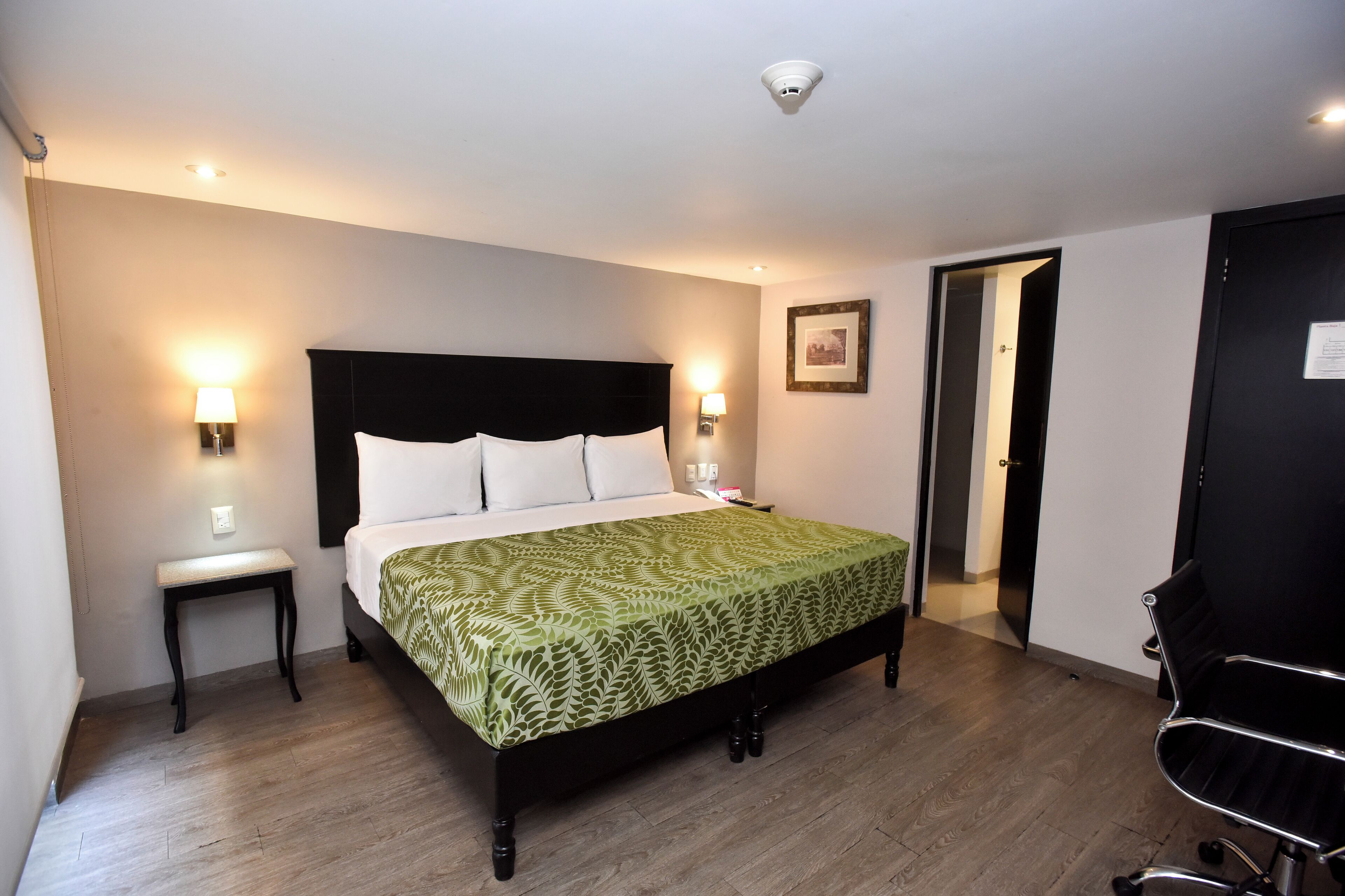 Een slaapkamer met een bed, nachtkastjes, een stoel en een deur.