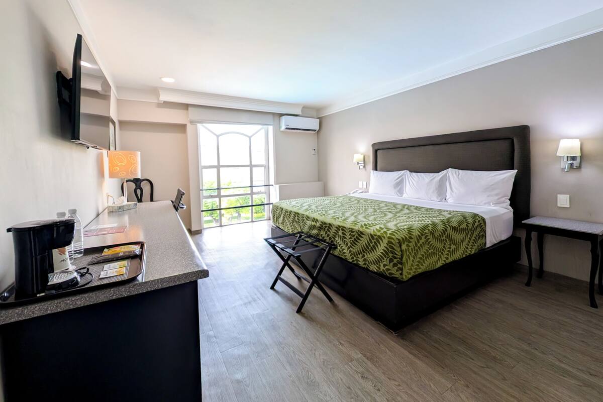 A hotel room with a bed, a desk, a chair, a TV, and a window.