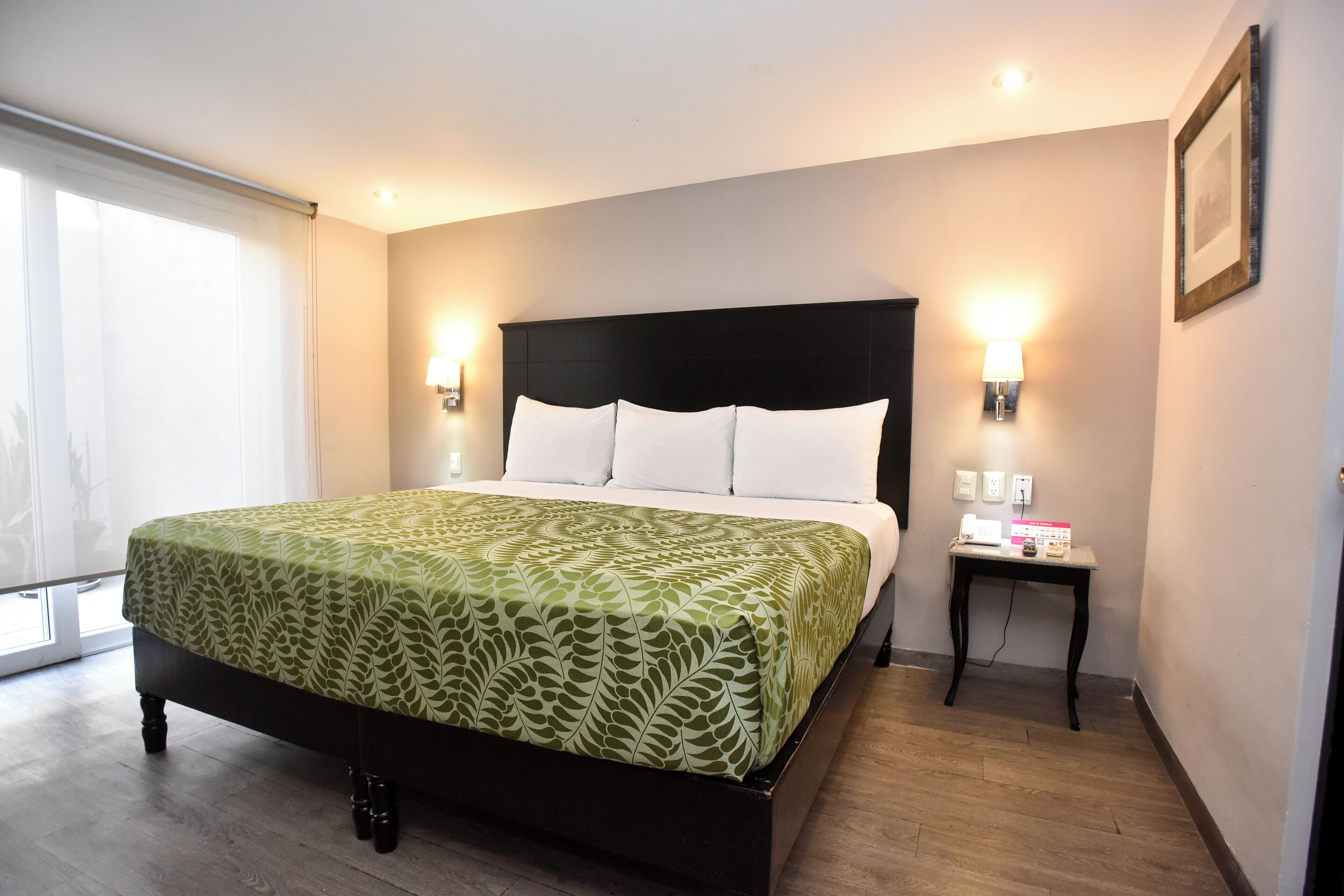 A neatly made bed with a patterned bedspread, a bedside table with a lamp, and a framed picture on the wall.