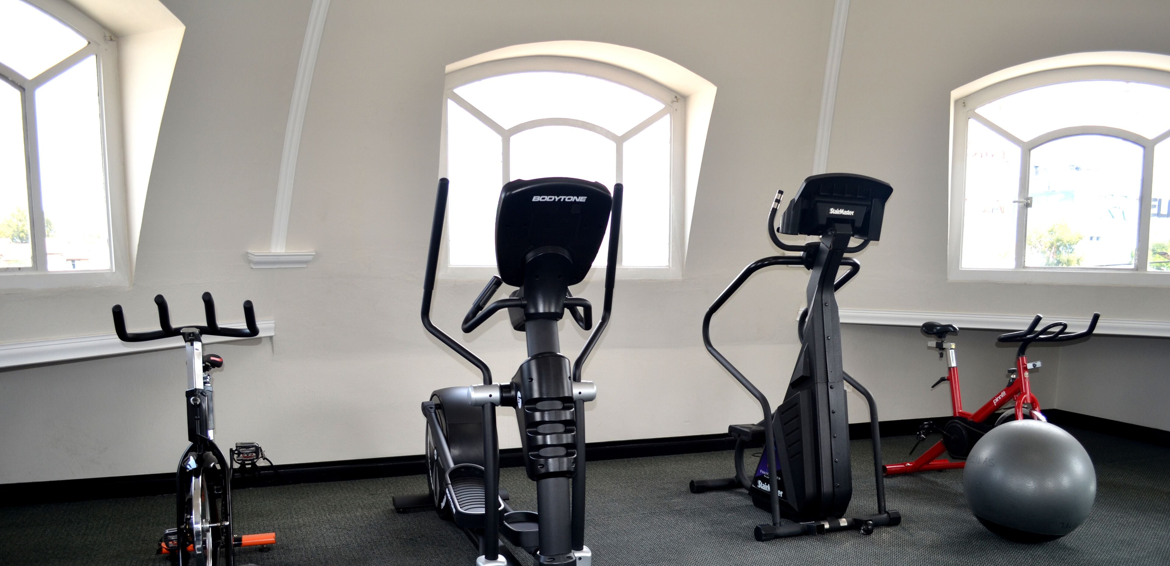 Une salle de sport intérieure équipée de matériel d’exercice, dotée de grandes fenêtres et comprenant un vélo d’appartement rouge.