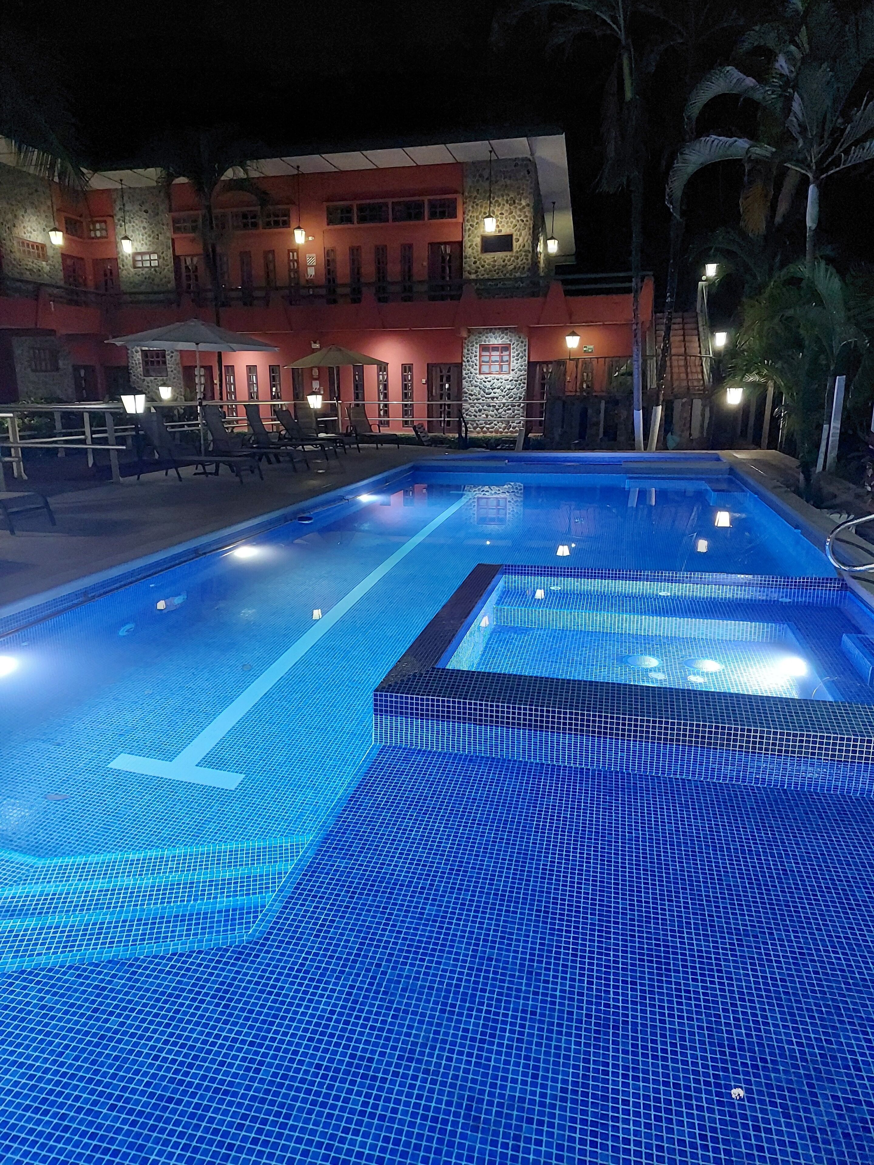 A swimming pool with a tiled deck and a building with a stone facade in the background.