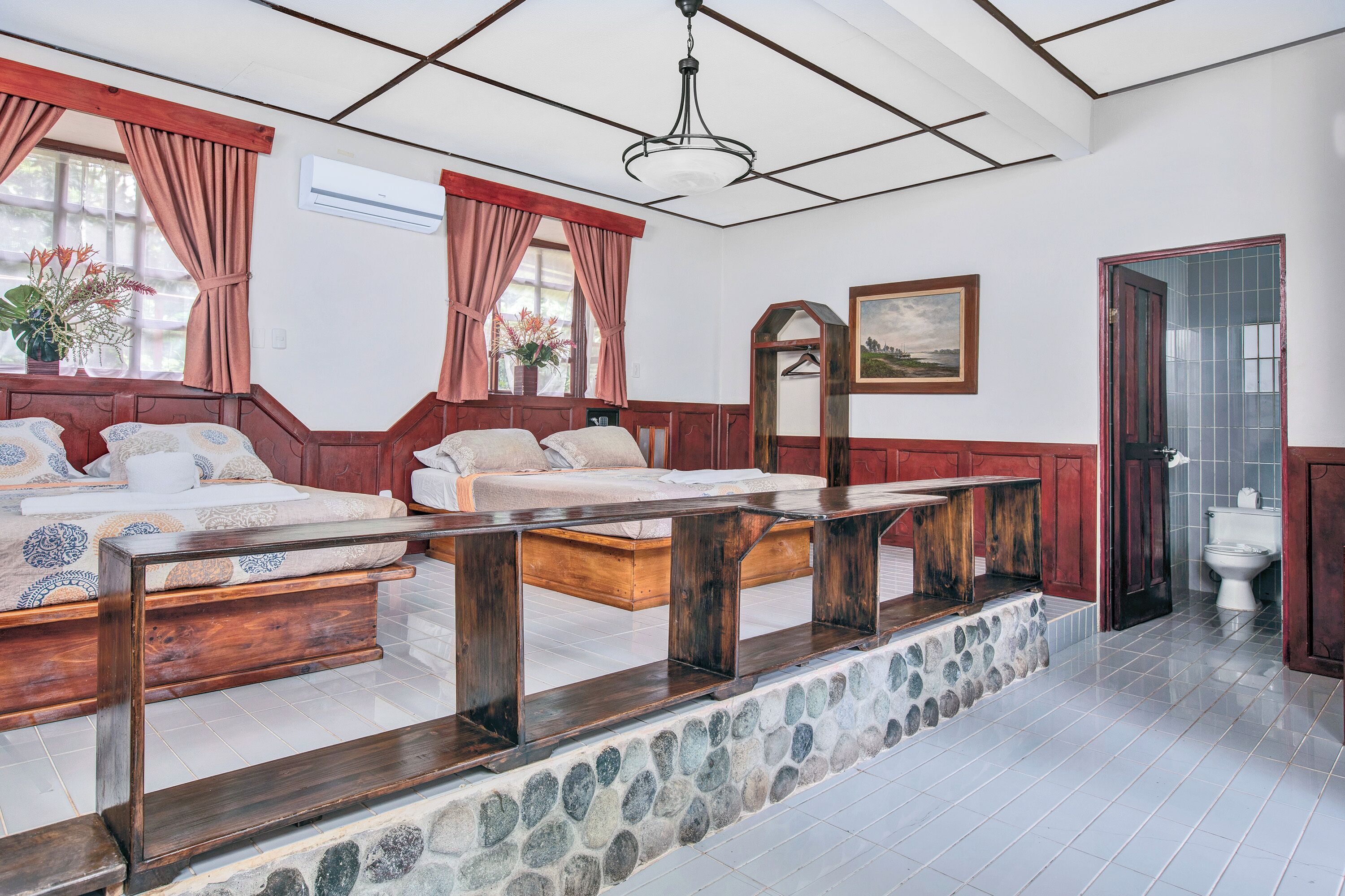 A bedroom with two beds, a stone wall, and a bathroom visible through an open door.