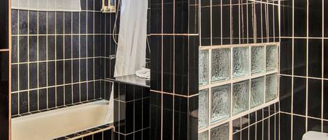 Ein Badezimmer mit schwarzen Fliesenwänden, einer weißen Badewanne und einer Dusche mit Glasabtrennung.