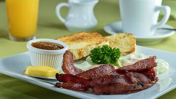 Un plato de desayuno con tostadas, tocino, huevos y un vaso de jugo de naranja.