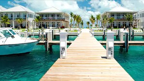 A marina with a wooden dock leading to a row of oceanfront buildings, boats docked, and palm trees. - Cape Eleuthera Resort & Marina (Freetown)