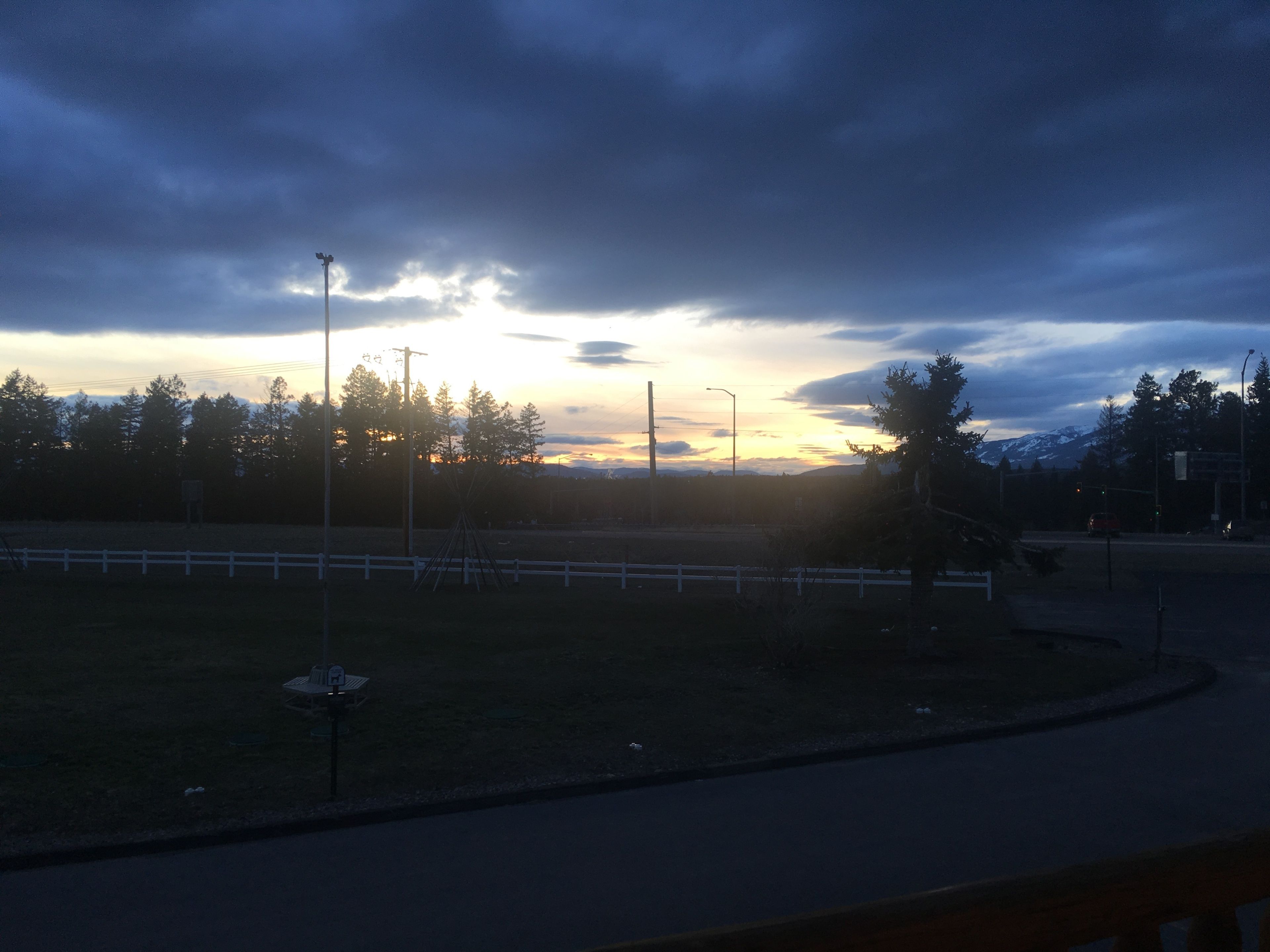 Zonsondergang met een weg, een wit hek en bomen.